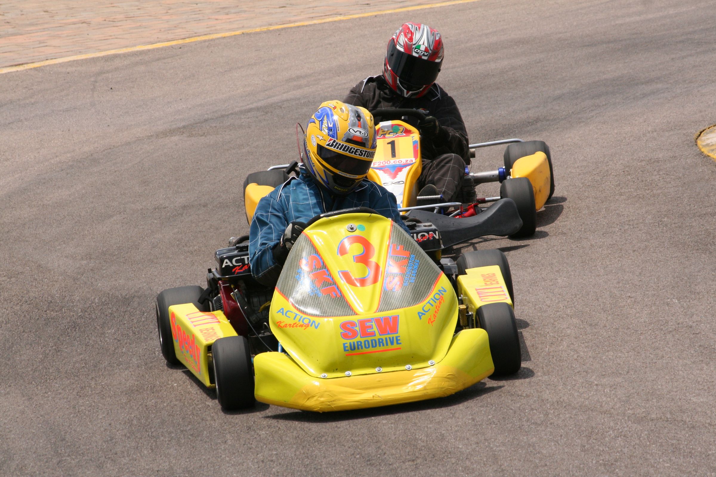 Two helmeted go-kart racers on an outdoor track