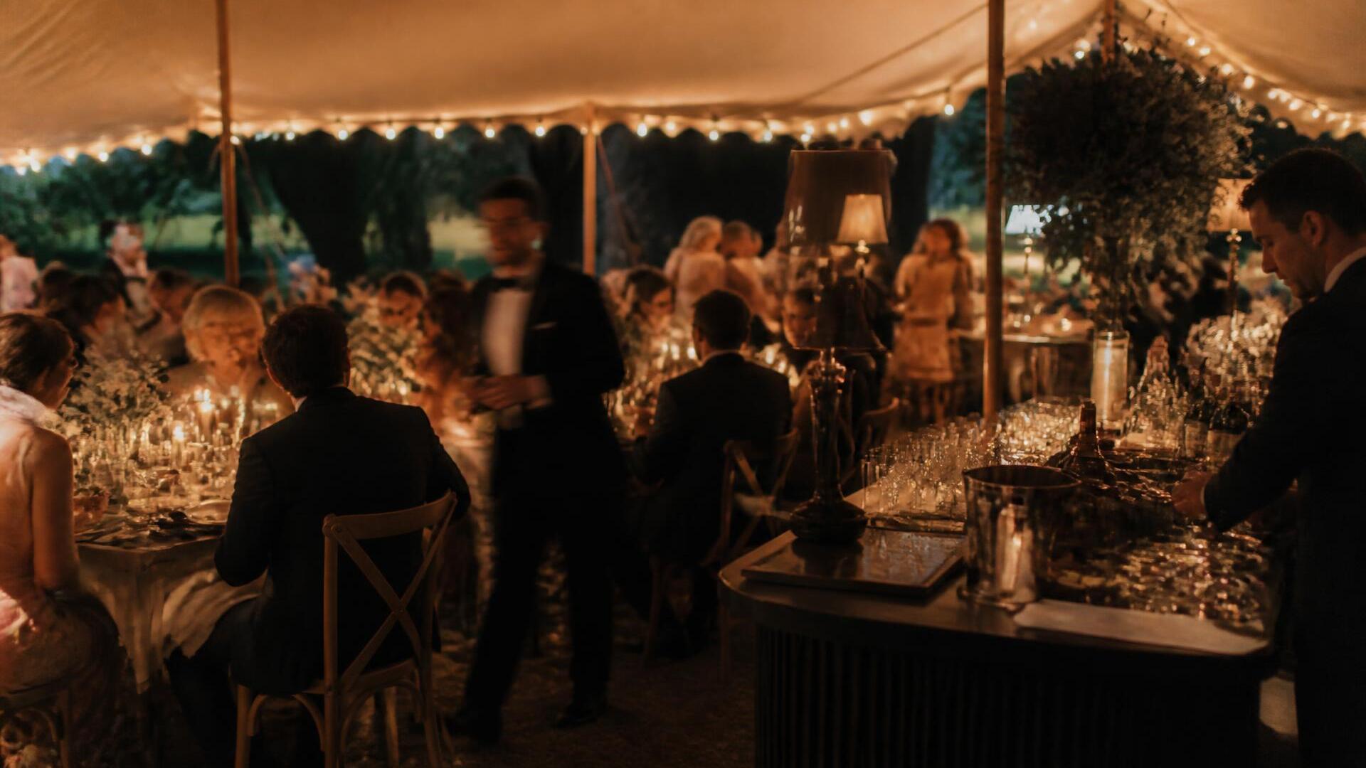 String lights and a long dinner table set for a warm evening backyard birthday celebration, glasses catching the last light